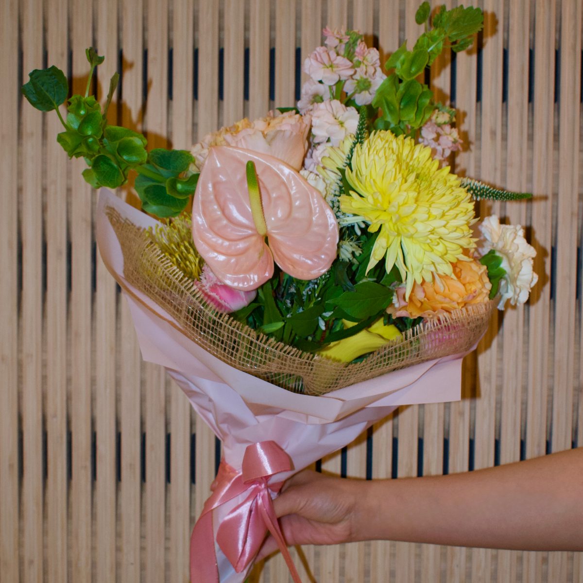 Hand-tied bouquet with anthurium, yellow chrysanthemum and stock, wrapped in blush paper with a satin bow
